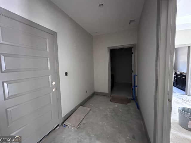 hall with unfinished concrete flooring, visible vents, and baseboards