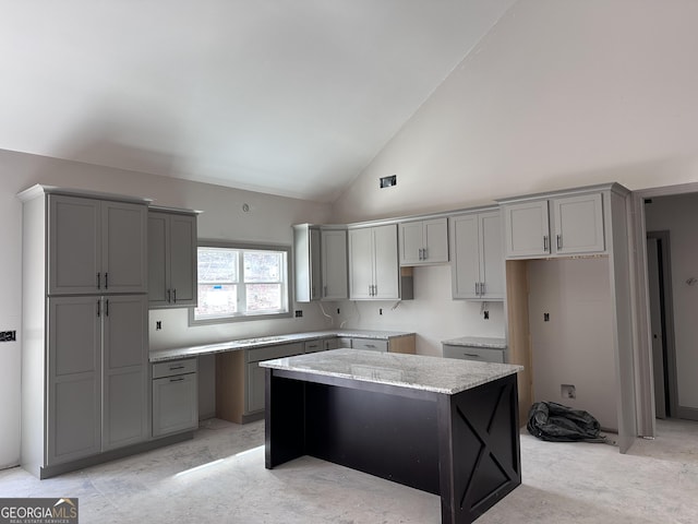 kitchen with high vaulted ceiling, a kitchen island, light stone counters, and gray cabinetry