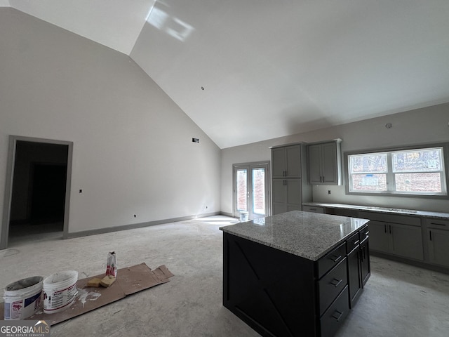 kitchen featuring open floor plan, a kitchen island, light stone countertops, high vaulted ceiling, and baseboards