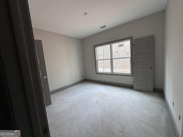 empty room with unfinished concrete floors, visible vents, and baseboards