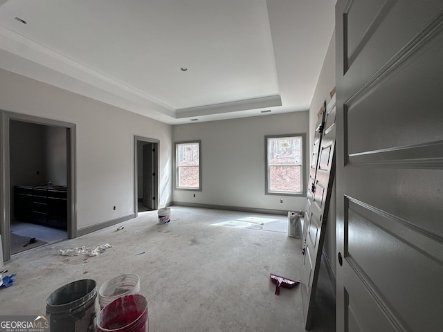 unfurnished bedroom featuring a barn door, baseboards, and a raised ceiling