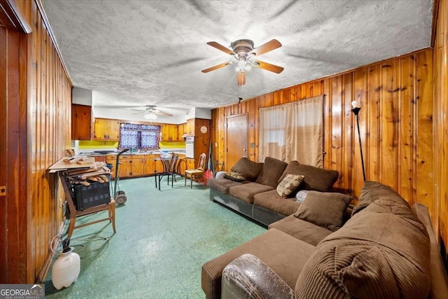 living room featuring ceiling fan, a textured ceiling, and wooden walls