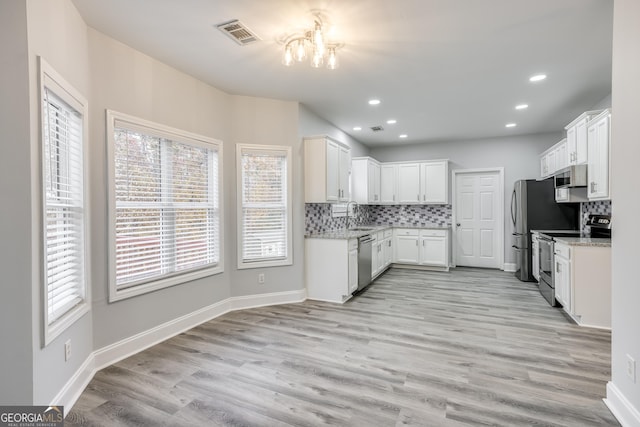 kitchen with light stone counters, backsplash, stainless steel appliances, and white cabinets