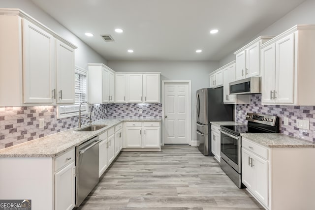 kitchen with sink, white cabinetry, light stone counters, light hardwood / wood-style flooring, and appliances with stainless steel finishes