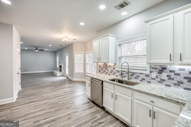 kitchen featuring white cabinetry, sink, stainless steel dishwasher, and light stone countertops