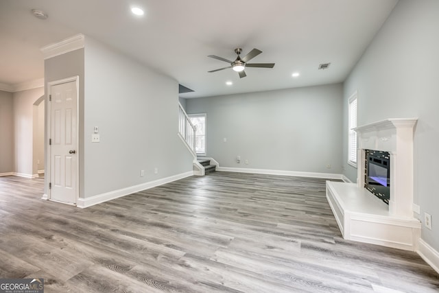 unfurnished living room with ceiling fan, crown molding, and light wood-type flooring