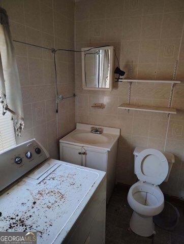 bathroom with toilet, vanity, tile walls, and washer / dryer