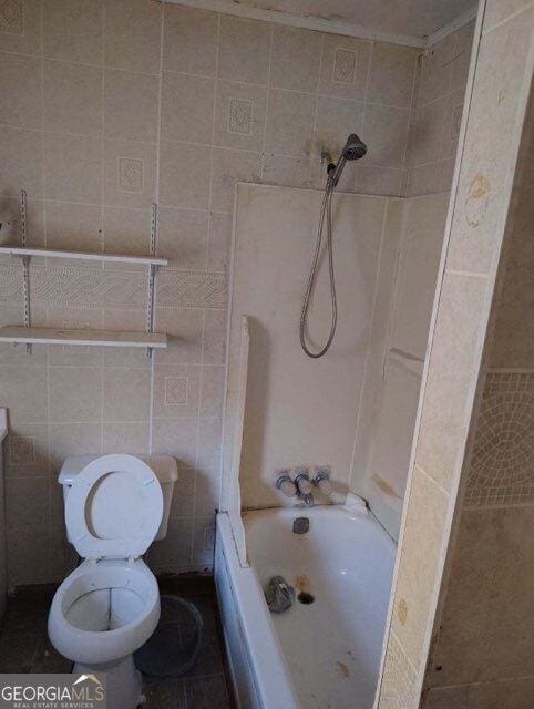 bathroom with tiled shower / bath combo, toilet, and tile walls