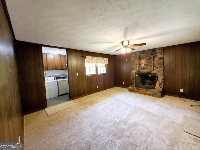 unfurnished living room with light colored carpet, ceiling fan, wooden walls, washer and dryer, and a fireplace