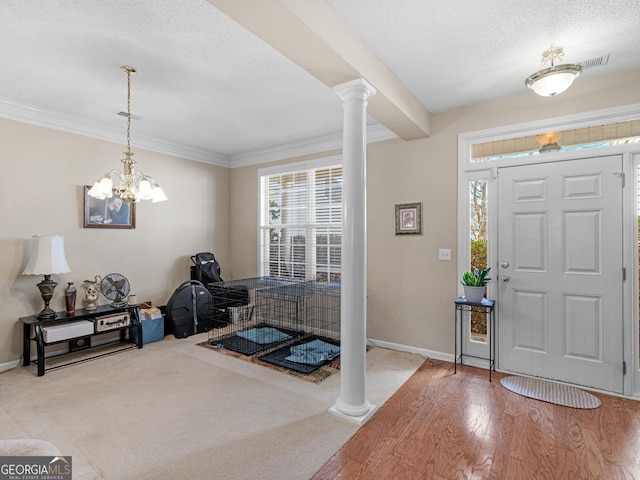 entrance foyer featuring an inviting chandelier, decorative columns, carpet floors, a textured ceiling, and ornamental molding