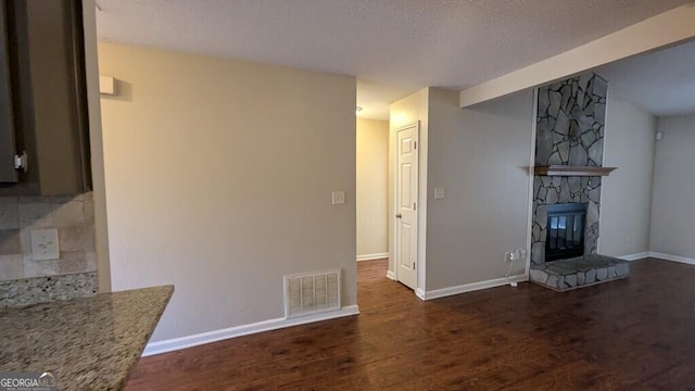 unfurnished living room with a fireplace, a textured ceiling, and dark hardwood / wood-style floors