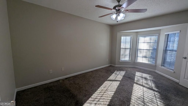 spare room featuring a textured ceiling, dark carpet, and ceiling fan