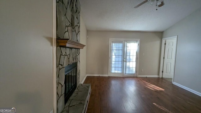 unfurnished living room featuring ceiling fan, french doors, dark hardwood / wood-style flooring, a textured ceiling, and a fireplace