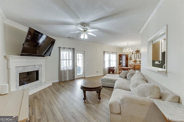 living room featuring a premium fireplace, light hardwood / wood-style flooring, crown molding, a textured ceiling, and ceiling fan with notable chandelier