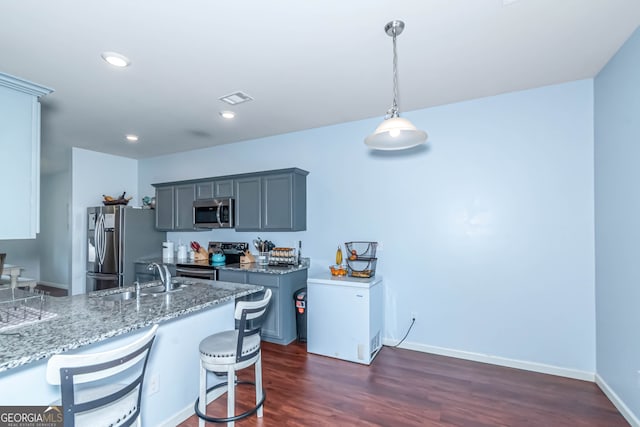 kitchen featuring dark wood-type flooring, sink, hanging light fixtures, light stone counters, and stainless steel appliances