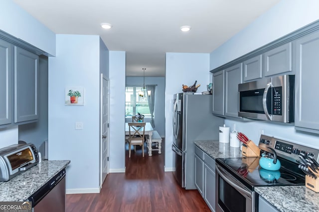 kitchen with stainless steel appliances, dark wood-type flooring, light stone counters, pendant lighting, and gray cabinets