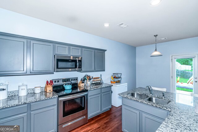 kitchen with appliances with stainless steel finishes, dark hardwood / wood-style flooring, light stone counters, sink, and pendant lighting