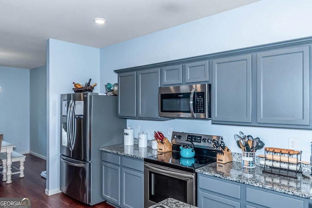 kitchen with gray cabinets, dark hardwood / wood-style flooring, dark stone counters, and appliances with stainless steel finishes