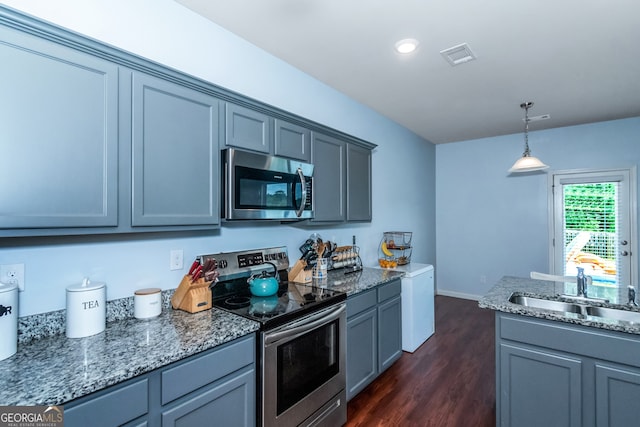 kitchen with appliances with stainless steel finishes, sink, decorative light fixtures, dark stone countertops, and dark hardwood / wood-style floors