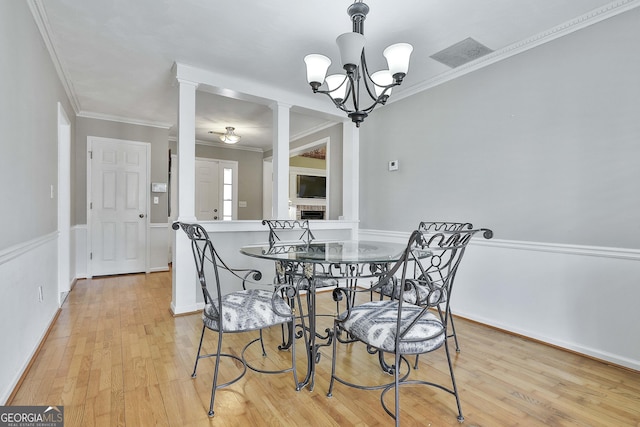 dining area with light wood-type flooring, ornamental molding, and a notable chandelier