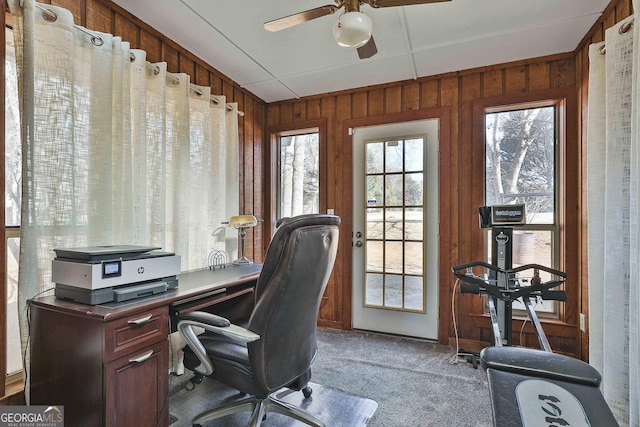 carpeted home office featuring ceiling fan and wood walls