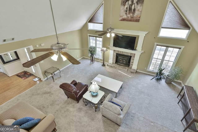 carpeted living room featuring a fireplace, a towering ceiling, ceiling fan, and a healthy amount of sunlight