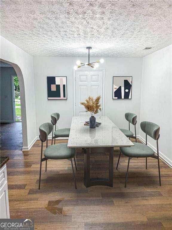 dining space with a textured ceiling, dark wood-type flooring, and a chandelier