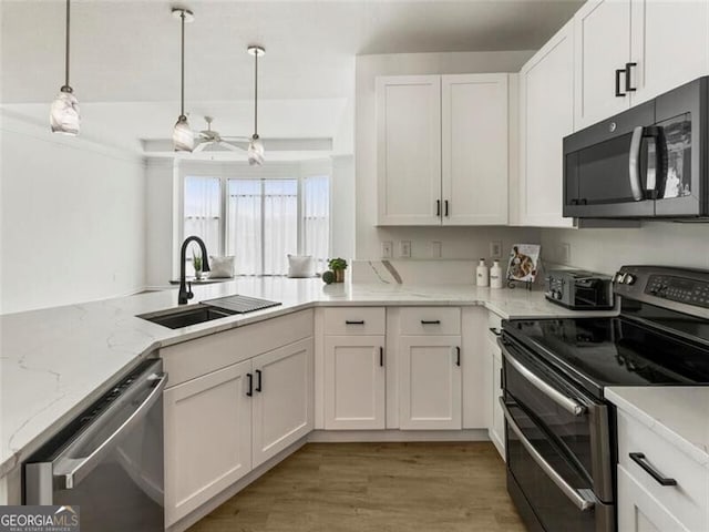 kitchen featuring light stone counters, stainless steel appliances, sink, pendant lighting, and white cabinets