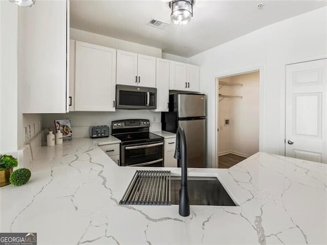 kitchen with light stone countertops, sink, white cabinets, and stainless steel appliances