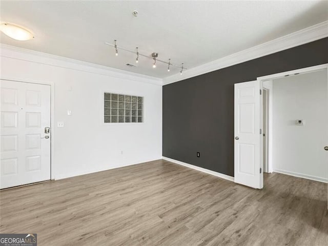 empty room featuring wood-type flooring, rail lighting, and ornamental molding