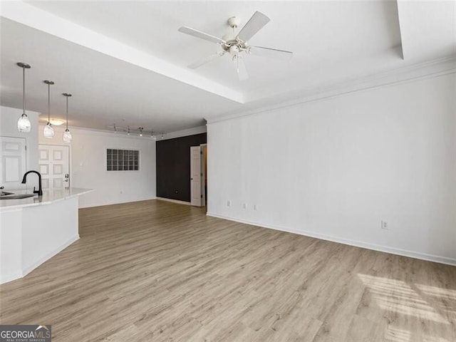 unfurnished living room with ceiling fan, light hardwood / wood-style floors, sink, and a tray ceiling