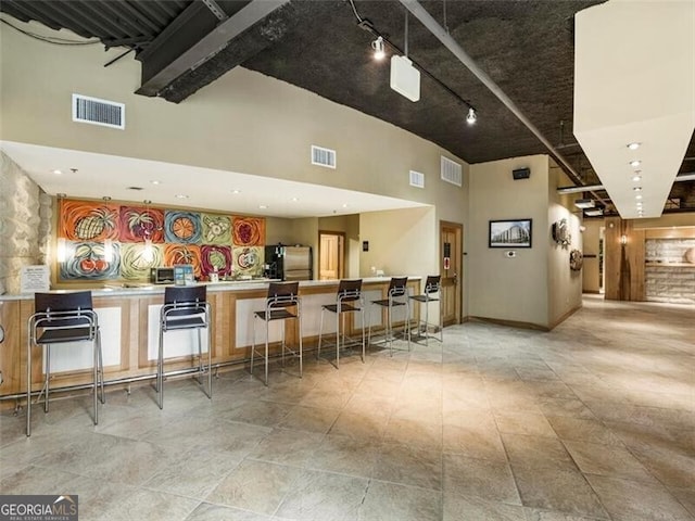 bar with stainless steel refrigerator and a towering ceiling