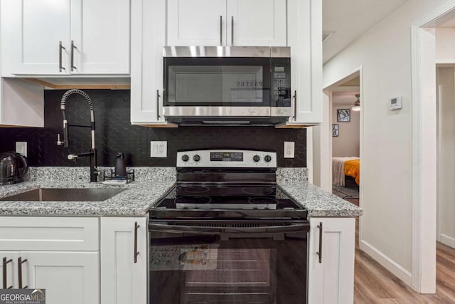 kitchen featuring white cabinets, light stone counters, sink, and black / electric stove