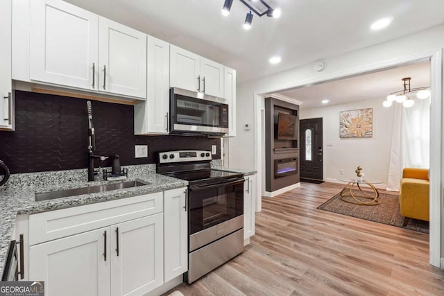 kitchen featuring appliances with stainless steel finishes, light wood-type flooring, tasteful backsplash, sink, and white cabinets