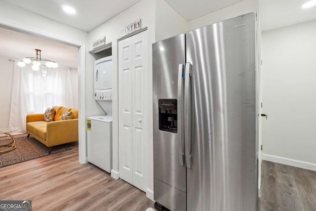 kitchen with stainless steel refrigerator with ice dispenser, light wood-type flooring, and stacked washer and dryer