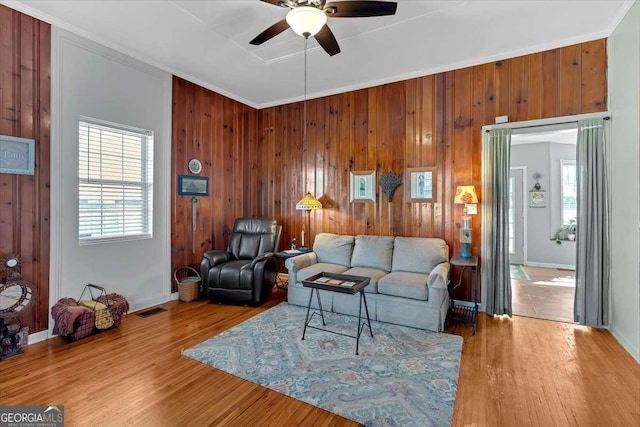 living area with wood finished floors, visible vents, baseboards, a ceiling fan, and crown molding