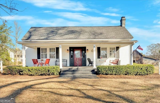 bungalow-style home with covered porch, a shingled roof, and a chimney