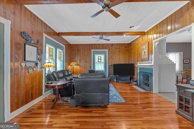 living room with ceiling fan, beamed ceiling, light wood-type flooring, and wooden walls