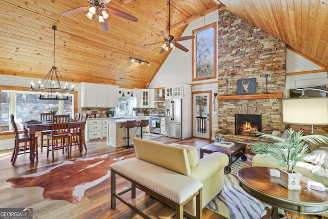 living room featuring a stone fireplace, high vaulted ceiling, light hardwood / wood-style floors, wood ceiling, and ceiling fan with notable chandelier