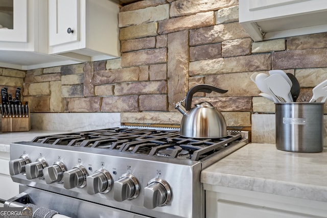 interior details featuring white cabinets, range, and backsplash