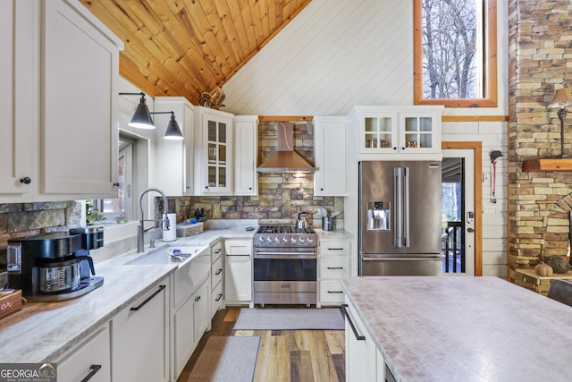 kitchen with high end appliances, sink, wall chimney exhaust hood, decorative light fixtures, and white cabinetry