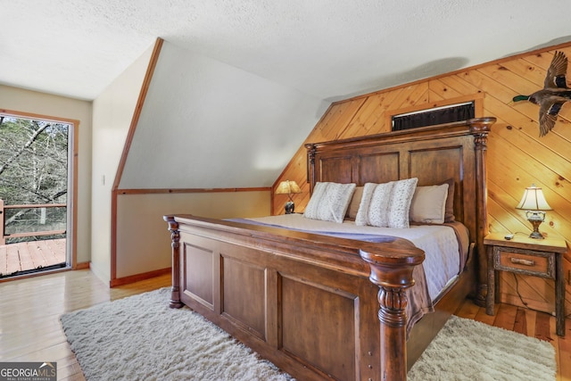 bedroom featuring lofted ceiling, light wood-type flooring, a textured ceiling, and wooden walls