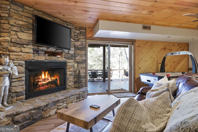 living room featuring light wood-type flooring, a stone fireplace, wooden walls, and wood ceiling