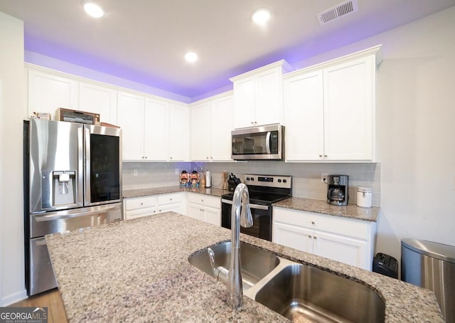 kitchen featuring white cabinets, stainless steel appliances, light stone counters, and tasteful backsplash