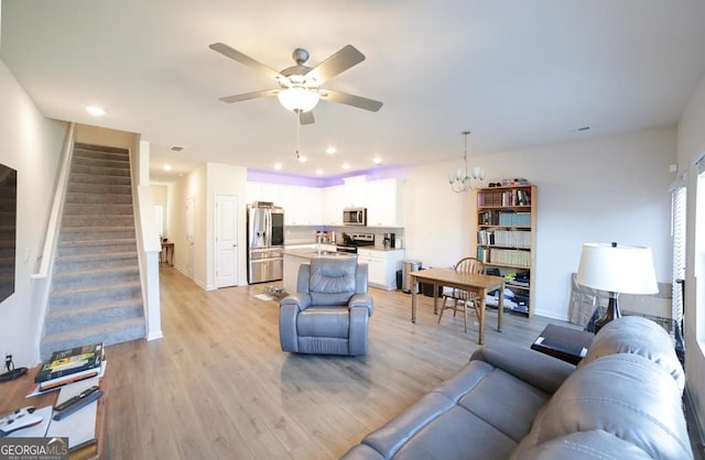 living room with ceiling fan with notable chandelier and light hardwood / wood-style floors