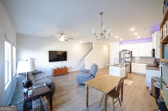 living room with ceiling fan with notable chandelier, light hardwood / wood-style flooring, and sink