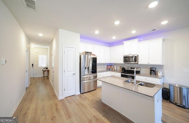 kitchen featuring appliances with stainless steel finishes, light stone counters, sink, a center island with sink, and white cabinetry