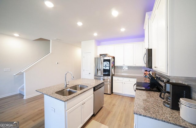 kitchen with a center island with sink, sink, light stone countertops, white cabinetry, and stainless steel appliances