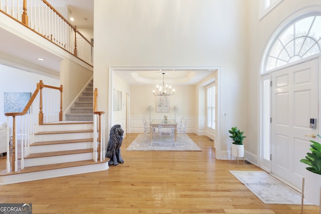 foyer with a chandelier, a raised ceiling, a towering ceiling, and light hardwood / wood-style flooring