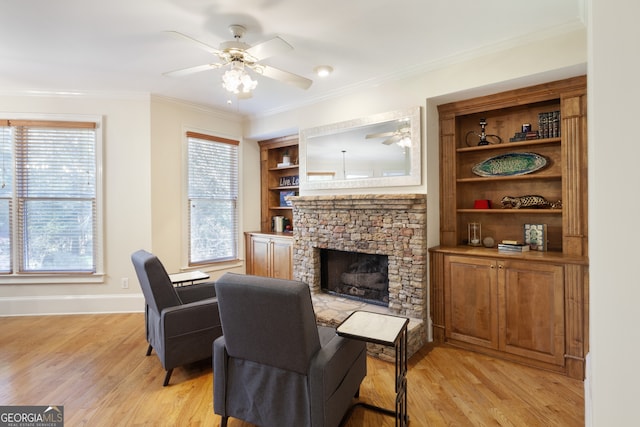 living room with ceiling fan, a stone fireplace, built in features, crown molding, and light hardwood / wood-style floors